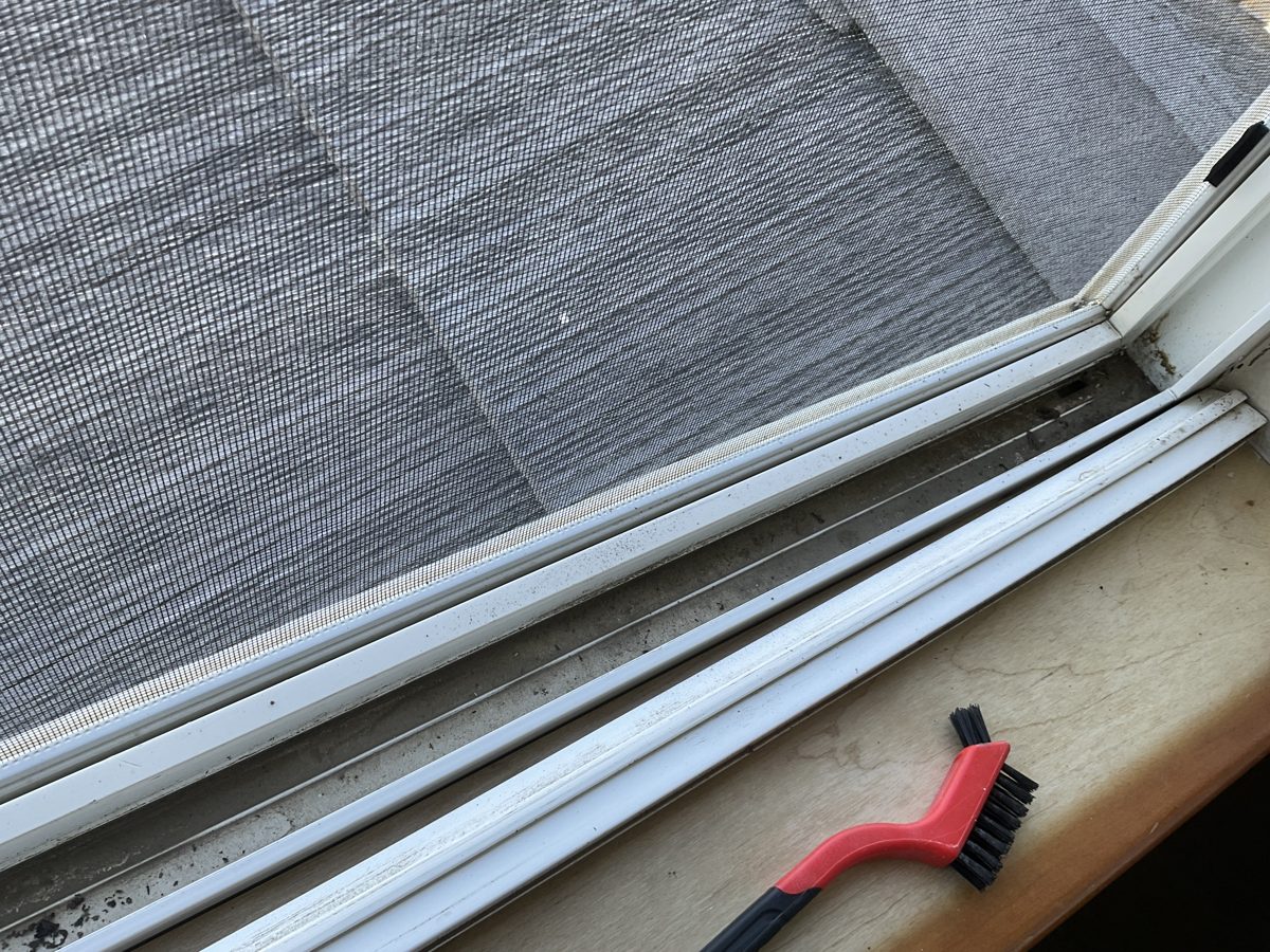 Detail brush working packed dirt out of a window track during a deep clean